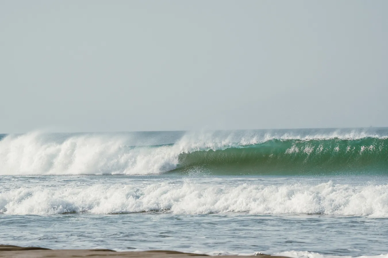 Onda verde quebrando em tubo, com a espuma branca levantando no vento.